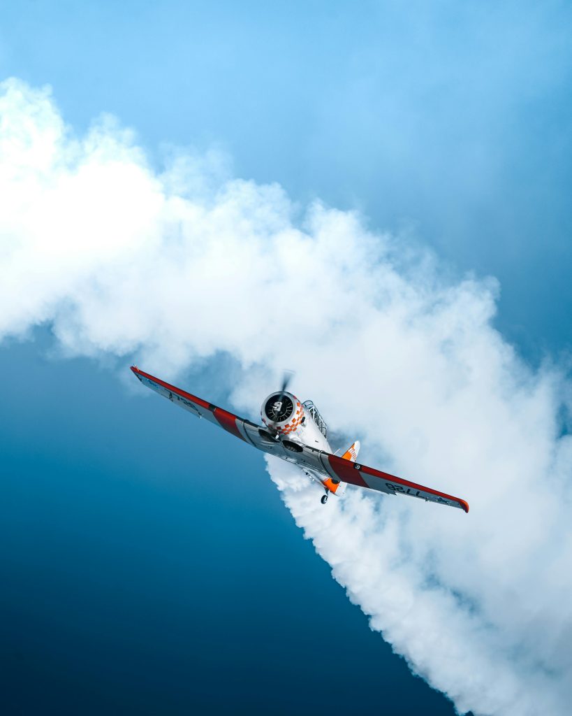 A sport plane performing aerobatics leaves a smoke trail against a vibrant blue sky.