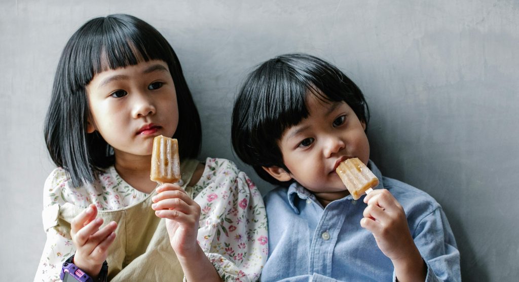 Cute moment of two children enjoying popsicles indoors, capturing childhood fun and friendship.